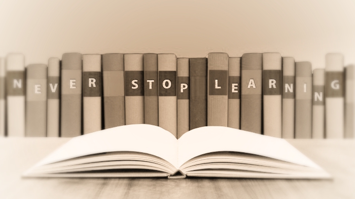 boook opened and the edge of many books behind spelling 'never stop learning'
